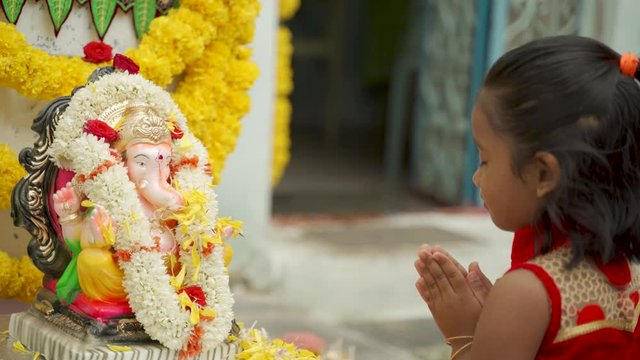 Little girl Kid offering flowers on Ganesha Idol before praying infront of god during Ganesha or vinayaka Chaturthi festival ceremony.