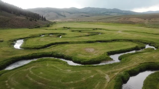 Sweeping aerial view of a creek meandering thru an alpine meadow valley in the Colorado Rocky Mountains on a cloudy day