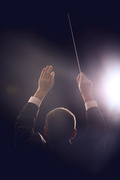 Male conductor on dark background, back view