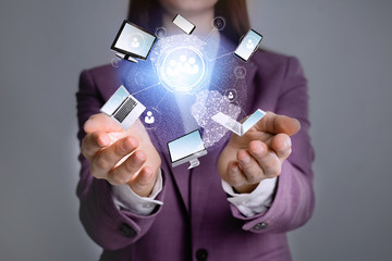 Young businesswoman holding digital image of Earth and different devices in hands on grey background, closeup