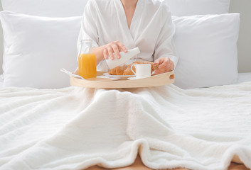 Young woman having breakfast on bed in hotel room