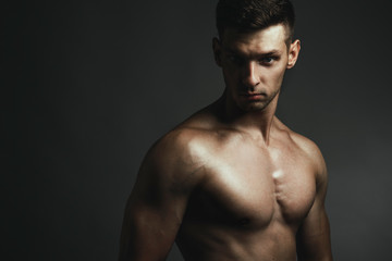 Fototapeta na wymiar Fitness body concept. Muscular young man posing over gray background. Perfect body. Close up. Studio shot