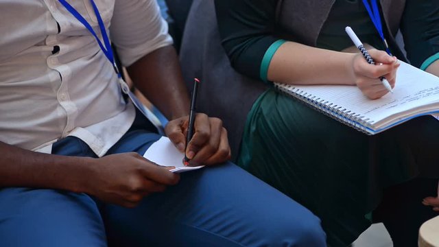 closeup people hands writing notes in notebook sitting in conference hall listening to lecture irrl. diverse people on a training. educating on training. professional business presentation advice