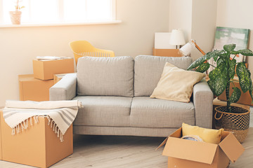 Cardboard boxes with belongings and sofa in new flat on moving day