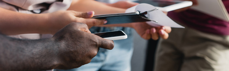 Panoramic crop of business people holding smartphone and clipboard in office
