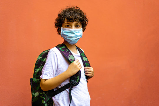 Cute elementary schoolboy with backpack going back to school during 2020 coronavirus (Covid-19) pandemic disease, kid wearing a protective face mask