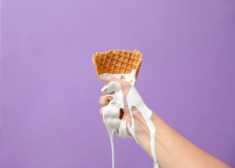 Woman holding crushed wafer cone with molten ice cream on violet background, closeup