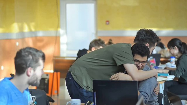 two men hug in coworking open space office, greeting friends irrl. colleagues embrace while working at laptop. college students team in coworking space. concept workplace, corporate