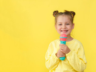 Lifestyle and people concept: a small, happy girl singing with a microphone, isolated by a bright yellow background.