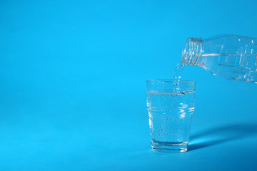 Pouring water from bottle into glass on blue background. Space for text