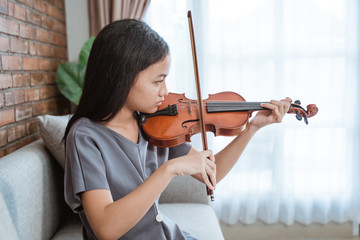 asian girl sitting on sofa holding violin takes out from violin case and testing with violin bow when indoors