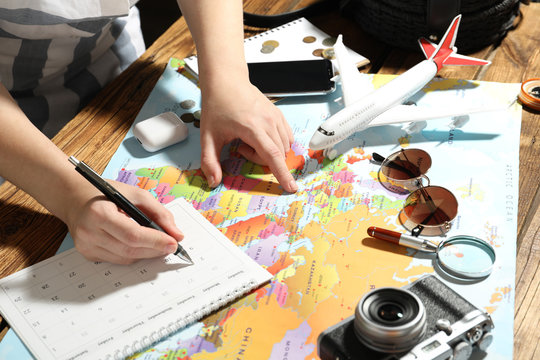 Woman marking calendar at table with world map, closeup. Travel during summer vacation - Powered by Adobe