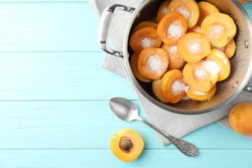Pot with apricots and sugar on light blue wooden table, space for text. Making delicious jam