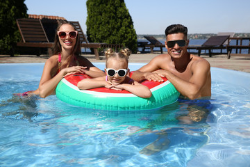 Happy family with inflatable ring in outdoor swimming pool on sunny summer day