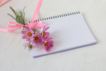 Notepad with a bouquet of delicate pink flowers, place for writing, top view