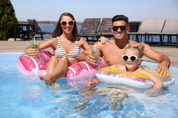 Happy family with inflatable rings and cocktails in outdoor swimming pool on sunny summer day