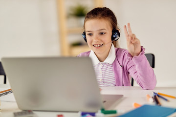 Happy schoolgirl raising arm to answer question while having online class from home.