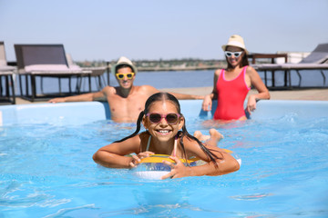 Fototapeta na wymiar Happy girl and her parents having fun in swimming pool. Family vacation