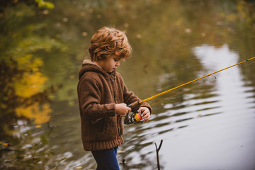 Little fisherman. Child boy fishing in overalls from a dock on lake or pond.