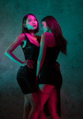 Portrait of two young cute Asian women in elegant dresses on the pink and yellow neon lights