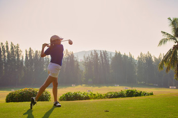 Young woman practices her golf swing on driving range, view from behind