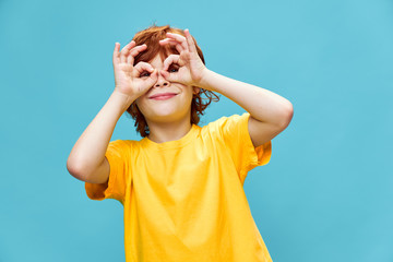 Happy boy in a yellow t-shirt holds joined fingers in front of his eyes 