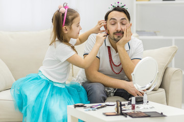 Obraz premium Cute little daughter and her handsome young dad in crowns are playing together.