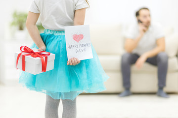 Photo of little girl hides present and postcard behind her back for her father.