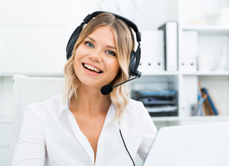 Young call center employee in headphones is sitting near laptop in the office. High quality photo