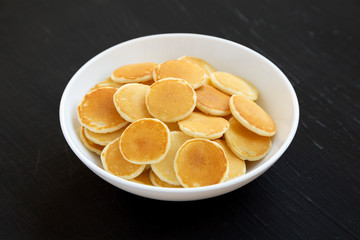 Homemade Mini Pancakes Cereal in a white bowl on a black surface, side view.