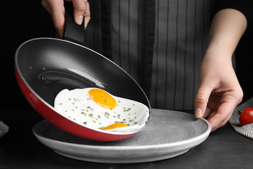 Woman putting tasty cooked eggs onto plate from frying pan at black table, closeup