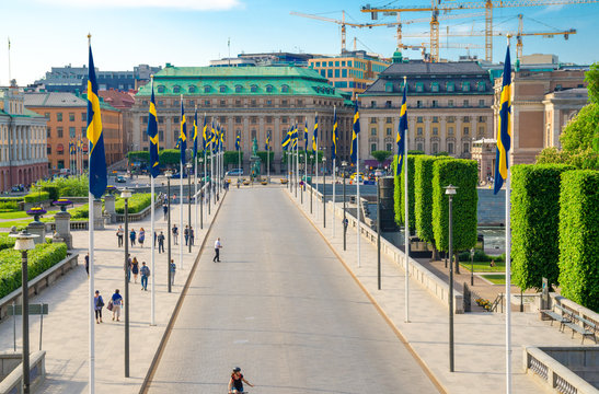 Sweden, Stockholm, May 29, 2018: Riksplan green grass lawn, bushes and street with national flags on Sodermalm island, Gustav Adolfs torg, Royal Swedish Opera house, blue sky with yellow cranes