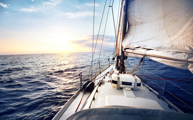 White sail yacht tilted in a wind at sunset. View from the deck to the bow, reefed sails, mast and...