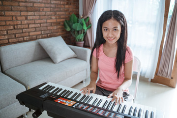 teenage girl in pink clothes learn to play a piano instrument while sitting in a room at home