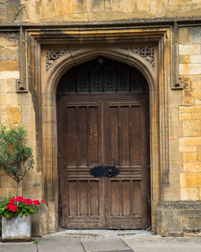 Large old arched door way with cast iron furniture.  Deep set doorway set into yellow stone building with plants and flowers outside