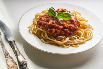 Traditional pasta bolognese served on a white plate and garnished with basil
