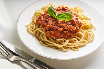 Traditional pasta bolognese served on a white plate and garnished with basil