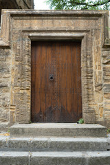 Old traditional heavy set wooden door with large stone arch around it and steps leading up to it.