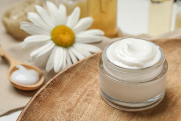 Obraz na płótnie Canvas Cosmetic cream and chamomile on table, closeup