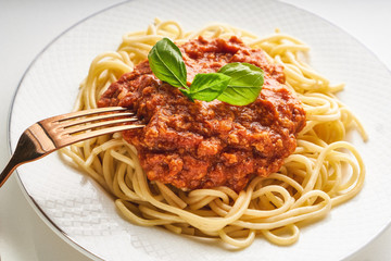Traditional pasta bolognese served on a white plate and garnished with basil