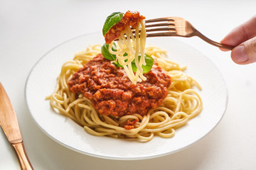 Portion Traditional pasta bolognese on a fork, served on a white plate and garnished with basil