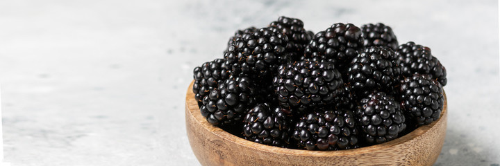 Dewberry. Blackberries in a wooden bowl on a light table. Fresh blackberries in a bowl close-up. Space for text. Banner