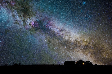 Colorful dust and gas clouds in the Milky Way on a summer sky with a house in the foreground with lights on in the window, Sweden