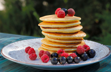 Pancakes. A stack of pancakes on a white plate garnished with raspberries and black currants. Food background. Horizontal, side view, close-up, free space.