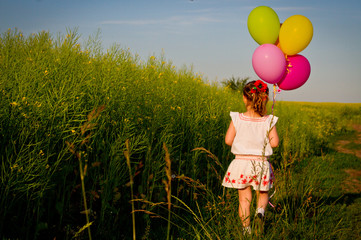 little Asian girl in a dress running through green wheat field with balloons in hand, slow motion.