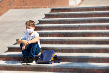 One student boy wearing mask is sitting on steps of stair beside his school during covid-19 pandemic time. New normal and education concept of coronavirus epidemic. Izhevsk, Udmurtia