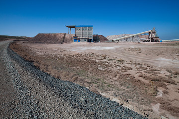 Obraz premium Mynaral, Kazakhstan: Jambyl Cement plant mine (quarry) for stone minerals, industrial building, conveyor and hopper on the clear blue sky in desert. Wide-angle panorama shot