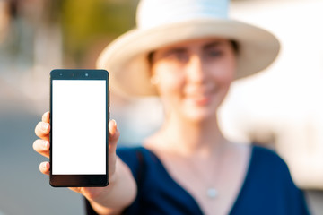 A woman in straw hat holds a smartphone in her hand, hand close-up. Portrait in a blur. Concept of modern technologies, business and applications for the phone