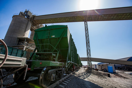 Mynaral/Kazakhstan: Jambyl Cement plant. Hopper cars on railway terminal. Rail wagons and loader conveyor on blue sky with sun background.