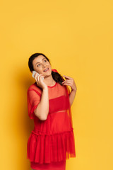  pregnant woman in red tunic looking up while talking on smartphone on yellow